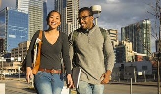 two students walking across CU Denver campus with the skyscrapers in the background